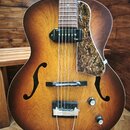 Polodupatá elektrická kytara s hnědým sunburst povrchem a dvěma f-otvory. Na krytu snímače je nápis Epiphone a na plechtru je vidět nápis Guild. Kyta…