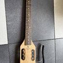 Světle hnědá elektrická kytara s krátkým tělem a dlouhým hnedým hmatníkem. Na těle je černý nápis TRAVELER GUITAR a nad ním logo ve tvaru trojúhelník…