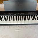 Černý digitální piano s klávesnicí a přikryvním víkem. Na víku i na ovládacím panelu je bílý nápis YAMAHA s logem značky. Na pravé straně ovládacího…