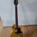 Žlutá elektrická kytara typu Les Paul s černým hmatníkem a černým pickguardem. Na hlavě je bílý nápis Epiphone a vpravo od něj nápis Les Paul. Nástro…