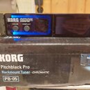 Na fotografii je rackový chromatický ladič a jeho originální krabice. Na přístroji i na krabici je bílé logo KORG a nápis pitchblack PRO RACKMOUNT TU…