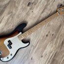 Elektrická basová kytara s tmelelovým povrchem v přechodu od černé k žluté barvě a bílým pickguardem. Na hlavě hmatníku je viditelné logo Fender. Nás…
