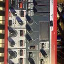 Detailní pohled na ovládací panel červeného syntetizátoru s nápisem SYNTH. Panel obsahuje zahlreiche knofíky, přepínače a popisky jako OSC PITCH, FIL…