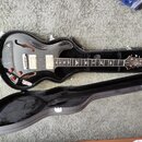 Černá polodubová elektrická kytara v černém tvrdém kufru. Na hmatníku jsou vložky ve tvaru ptáků a na hlavě je viditelné logo Epiphone. Tělo má leskl…