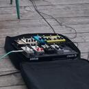 Černý pedalboard značky pedaltrain model classic s několika efektovými pedály. V horní řadě jsou umístěny tři pedály v bílé, modré a žluté barvě. Spo…