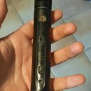 Detailní pohled na černý mikrofon v ruce. Na těle je viditelné logo ve tvaru stylizovaného písmene G v kruhu a nápis AUTHENTICA. Jsou zde přepínače s…
