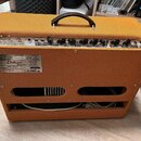 Kytarový kombozesilovač s oranžovým texturovaným potahem a černou rukojetí. Na zadním panelu je štítek s nápisy Blues -Deluxe™ Reissue a sériovým čís…