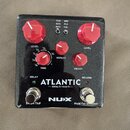 Efektový pedál s černým třpytivým povrchem a červenými oválnými knoflíky. Na zařízení jsou nápisy ATLANTIC — delay & reverb —, NUX, Smart TAP a Hold…