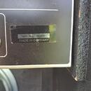 Detailní záběr na zadní část černého elektronického zařízení. Na povrchu je nalepený stříbrný štítek s nápisy SER. NO 233920 a MADE IN GERMANY. Povrc…