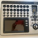 Digitální mixážní pult stříbrné barvy s černým displejem a ovládacími prvky. V pravém horním rohu je nápis QSC TouchMix-16. Na zadním panelu jsou vid…
