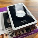 Stříbrné audio rozhraní s černým lesklým horním panelem a velkým kovovým oválovým knoflíkem. Na povrchu je bílý nápis duet by APOGEE. Zařizení leží n…