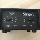 Černý přístroj v texturovaném obalu s nápisy Tube Amp Doctor™ a Silencer™. Přední panel obsahuje dva ovratové ovládací knoflíky, červenou kontrolku P…