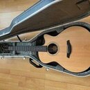 Akustická kytara s přírodním dřevem a tmavým hmatníkem v otevřeném tvrdém kufru. Na hlavě nástroje je viditelné logo, které je však nečitelné. Povrch…