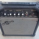 Černý kytarový kombozesilovač v plastovém kufru s rukojetí. Na horním ovládacím panelu jsou nápisy DRIVE, MASTER, EQUALIZATION, GUITAR AMP, INPUT, GA…