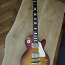 Elektrická kytara typu Les Paul s barevným přechodem od žluté přes červenou k hnědé. Na hlavě hmatníku je nápis Luxury a na krku u první pražnice ozn…
