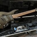 Černá elektrická kytara s hnědým hmatníkem v černém tvrdém kufru. Na hlavě nástroje je bílé logo Jackson. Kytara má dva humbuckery, prohnutý most a v…