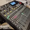 Digitální mixážní pult černé barvy s nápisem X32 PRODUCER. Zařízení obsahuje displej, zahlreiche posuvníky, tlačítka a otočné ovladače. Na panelu jso…