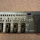 Šedý multifektoped Boss ME-80 Guitar Multiple Effects. Zařízení obsahuje řadu ovládacích knofíků, přepínačů a čtyřistupňové displeje s nápisy jako PR…