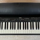 Černý digitální piano s klávesnicí. Na horním panelu a na krytu je bílý nápis YAMAHA. V pravé části ovládacího panelu je uveden model P-85. Povrch kr…