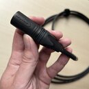 Černý kabel s konektorem značky NEUTRIK. Na plastovém krytu je vyražen nápis NEUTRIK a v další části je viditelný neúplný nápis ONEUTR. Povrch konekt…