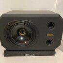 Černý studiový monitor umístěný na černém podstavci. Na reproduktoru je viditelný nápis TANNOY a pod ním označení SYSTEM 600. Podstavec nese bílý náp…