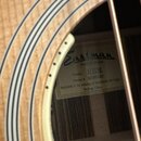 Detail akustické kytary se zaměřením na vnitřní štítek u ozvukové otvory. Na bílém štítku je černé logo Eastman a nápisy Handcrafted Guitar, Model E3…