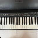 Černý digitální klavír značky YAMAHA. Na ovládacím panelu jsou umístěny různé tlačítka a posuvníky s nápisy jako MASTER VOLUME, METRONOME, SONG, VOIC…