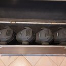 V otevřeném transportním kufru jsou vedle sebe umístěny čtyři černé svítící hlavy nebo efektové lampy. Na každém zařízení je zepředu viditelný nápis…