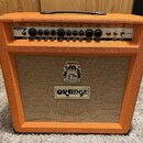 Kytarový kombozesilovač v oranžovém vinylu s hnědým textilním předním krytem. Na ovládacím panelu je nápis ORANGE a modelové označení ROCKERVERB 30 M…