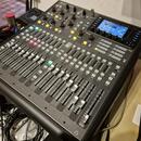 Digitální mixážní pult v černé barvě s kovovým šasi. V horní části je displej a nápis X32 Producer. Ovládání tvoří řada posuvníků, tlačítek a otočnýc…