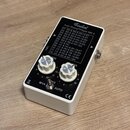 Bílý efekt pedál s černým horním panelem. Na vrchu je nápis Ginbol a model Auto Stomp® Player MK II spolu s tabulkou nastavení čísel 01 až 12. Pedál…