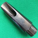 Stříbrný kovový mouthpiece s nápisem v horní části, který je nečitelný. Povrch vykazuje drobné škrábance a známky opotřebení. Nástroj leží na zeleném…
