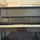Černý pianino s klaviaturou z bílých a černých kláves. Na přední části nad klaviaturou je zlatý nápis AUGUST FÖRSTER. Povrch nástroje vykazuje známky…