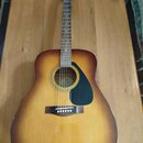 Akustická kytara s tělem tvaru dreadnought a barevným přechodem od žluté k tmavě hnědé (sunburst). Na hlavě je bílý nápis YAMAHA. Kytara má černý ple…
