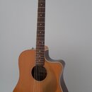 Akustická kytara s cutawayem v přirozené dřevěné barvě a tmavě hnědými boky. Na hlavě hmatníku je viditelné logo "Fender". Nástroj stojí na černém st…