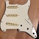 Bílá plechová pickguard pro elektrickou kytaru s třemi nasazenými snímači s krémovými plastovými krytkami. Povrch je hladký a glossy, s několika vidi…