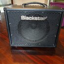 Černý kytarový kombozesilovač s povrchem z textilie a kovovou ochrannou mřížkou reproduktoru. Na mřížce je umístěno bílé logo Blackstar. Nástroj má v…