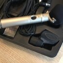Stříbrný mikrofon s černou větrnou clonou v černém přepravním kufru. Na těle mikrofonu je nápis RØDE NT1. V kufru se nachází také černý kabel a černé…