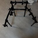 Černý kovový stojan na bicí nástroje s několika nastavitelnými rameny a úchytmi. Konstrukce obsahuje řadu utahovacích šroubů s knoflíky pro fixaci po…