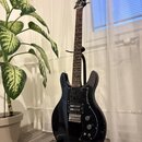 Černá elektrická kytara s tmavým hmatníkem, umístěná na stojanu. Na hlavě je bílý nápis "Epiphone". Tělo má dva humbuckery, jeden ovládací knoflík a…