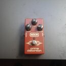 Červený efekt pedál s třemi černými ovládacími knoflíky. Na zařízení jsou nápisy OUTPUT, TONE a DISTORTION, logo MXR v bílém obdélníku a text prime d…