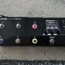 Černý kytarový procesor s nápisy LINE 6 HX STOMP XL. Zařízení má osm stomečů, tři otočné knoflíky a displej s textem 24A BASCNTR Pro, Ampeg Scrambler…