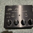 Černý analogový emulátor cabinetů s nápisy „Sub“ a „AXE“. Na předním panelu je text „ANALOG CABINET EMULATOR“, kontrolky „POWER“ a „CLIP“ a čtyři čer…