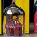 Skleněná elektronka s kovovými kontakty v dolní části. Na skle je červený nápis ECO83S a červené kulaté logo s vlnovkou. V pozadí je vidět modrožluté…