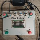 Kytarový předzesilovač v bílém provedení s nápisem Blackstar a označením HT-DUAL. Zařízení má v horní části šest otočných ovladačů s popisky GAIN 2,…
