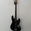 Černá elektrická basová kytara s tmavým hmatníkem a světlou hlavou. Na hlavě je viditelné logo "Squier". Nástroj je v dobrém vizuálním stavu a visí n…