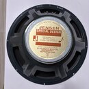 Fotografie znázorňuje zadní stranu reproduktoru s černým kovovým rámem. Uprostřed je nalepená kulatá štítková nálepka s nápisy „JENSEN MUSIC INDUSTRI…