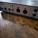Detailní pohled na zadní panel stříbrného USB audio rozhraní s černým rámem. Na zařízení jsou nápisy UR-RT2, USB AUDIO INTERFACE a 24 bit/192kHz D-PR…