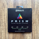 Černá krabička s hudebními strunami. Na povrchu je bílé logo D'Addario, barevný trojúhelník a nápisy PRISM™, ULTRA BRIGHT STRINGS, .050 .070 .085 .10…