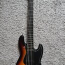 Elektrická basová kytara s tmeňem v barevné gradaci od žluté přes oranžovou po černou. Nástroj má černý pickguard, čtyři struny a světlý dřevěný hmat…